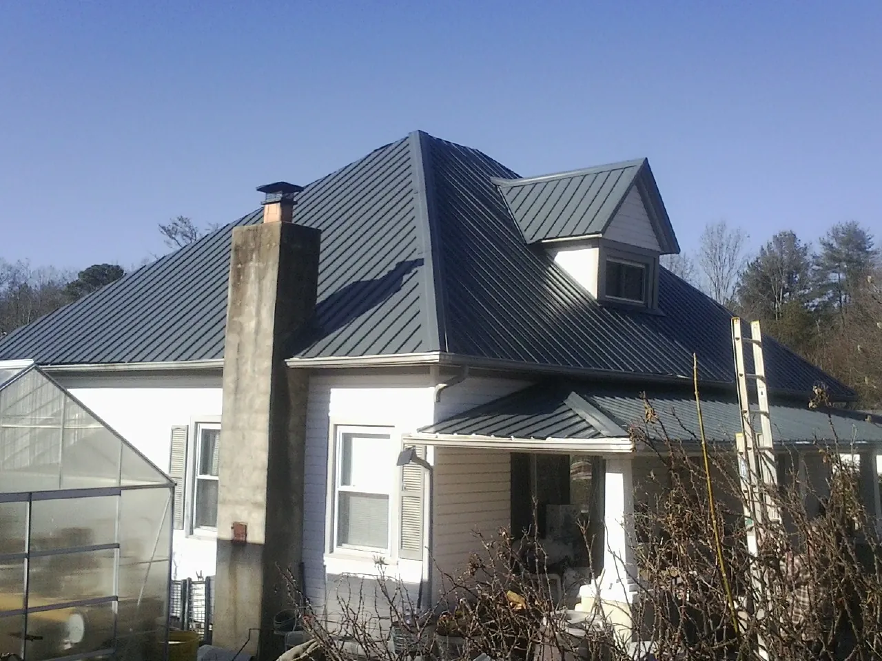 Dark blue standing seam metal roof on a white farmhouse with dormer — Slate & Tile Roof Repair by Roofing Brothers in Los Lunas
