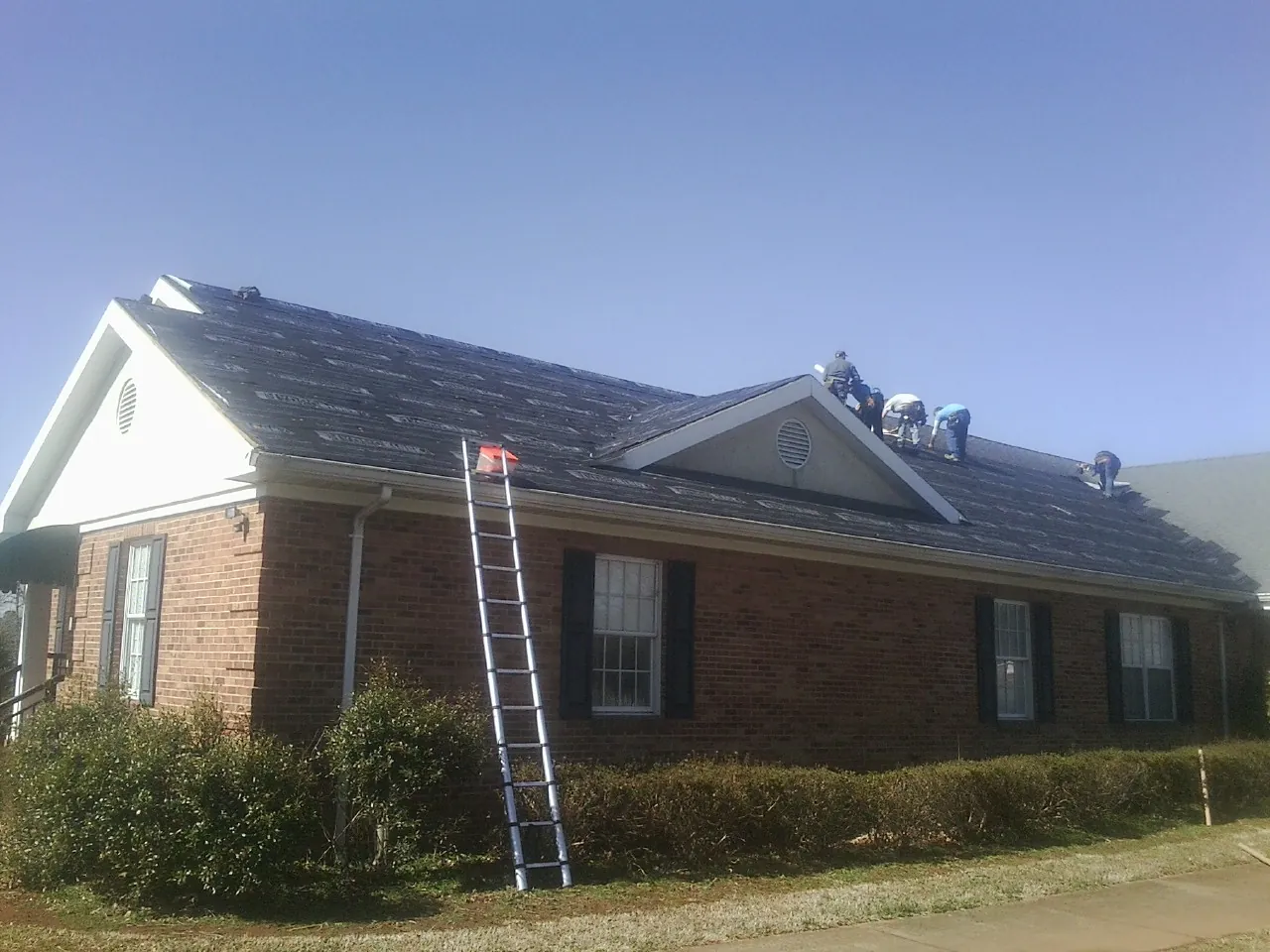Crew tearing shingles off a brick ranch roof with a ladder set — Metal Roof Repair work by our crew in Los Lunas