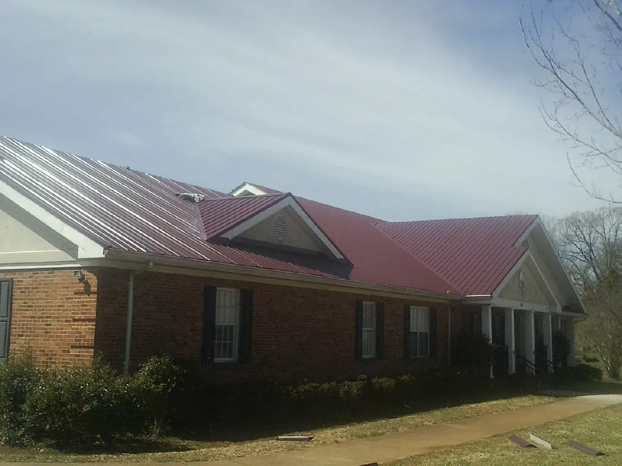 Red metal roof with gabled entries on a long brick building, from a Hail Damage Roof Repair job in Los Lunas