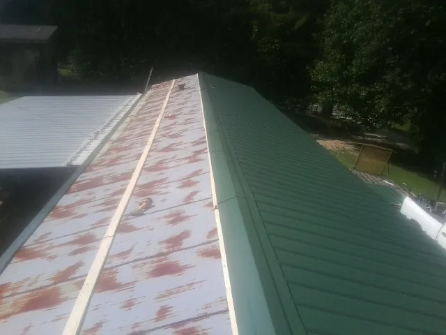 Old rusted panels beside newly installed green metal roofing — Wind Damage Roof Repair by Roofing Brothers in Los Lunas