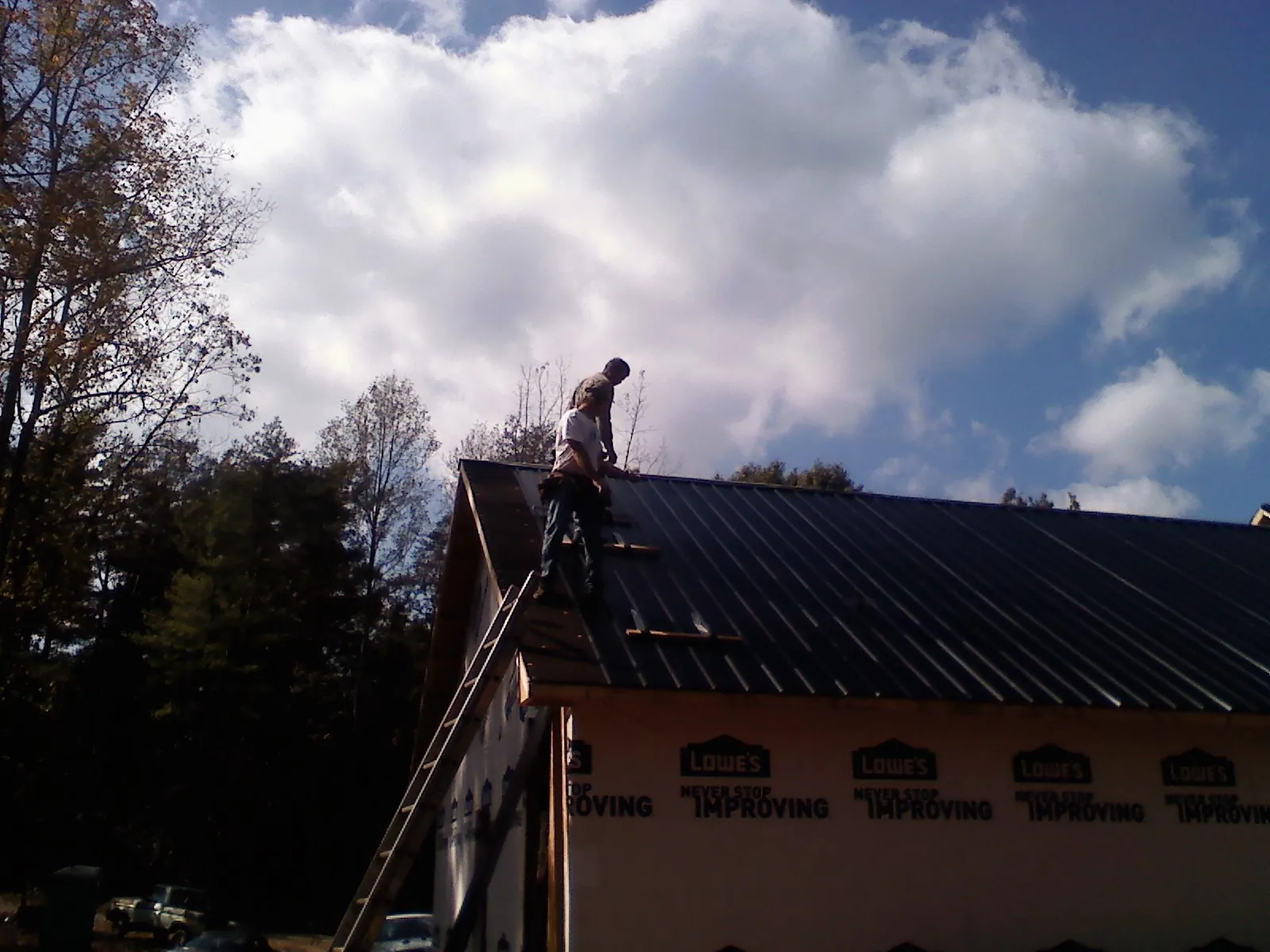 Roofer fastening dark metal panels high against a cloudy sky, from a Roof Inspection job in Los Lunas
