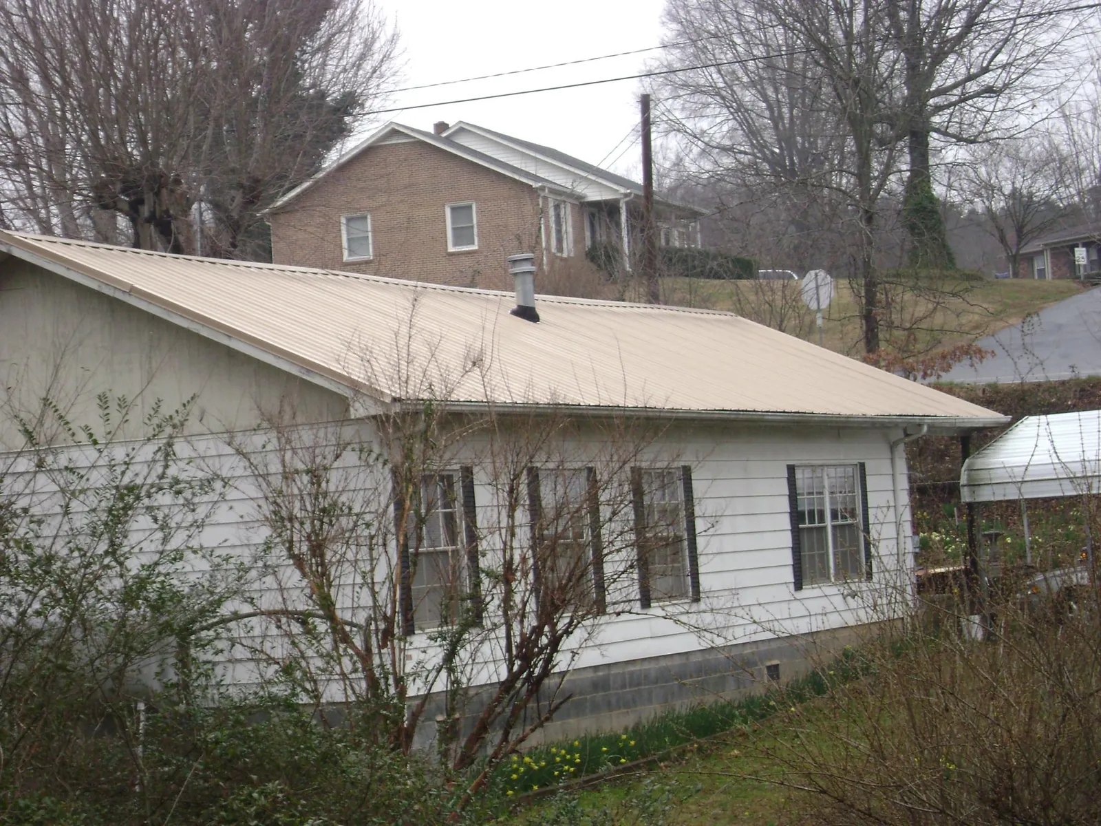 Tan metal roof on a white sided house set into a hillside — Commercial Roofing by Roofing Brothers in Los Lunas